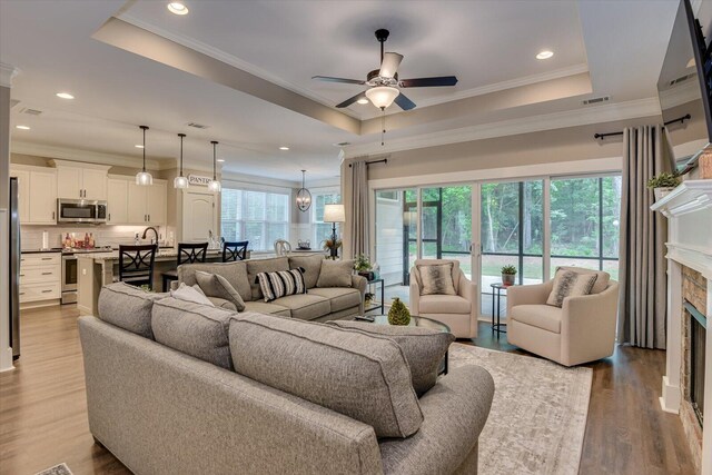 living room with a tray ceiling, light hardwood / wood-style flooring, ceiling fan, and crown molding