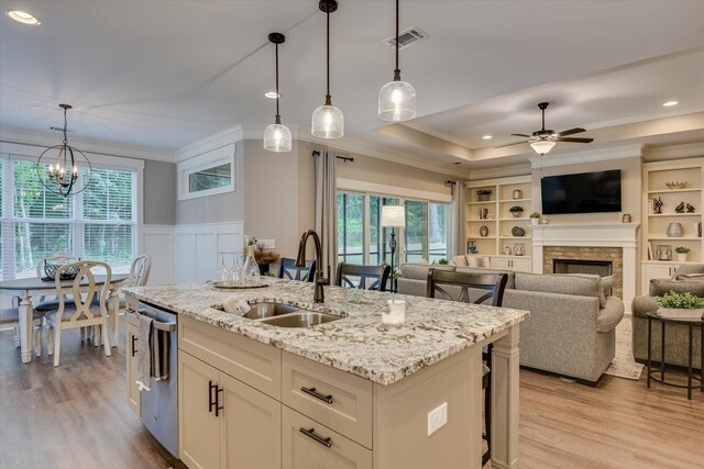 kitchen featuring stainless steel dishwasher, a kitchen island with sink, sink, pendant lighting, and a fireplace