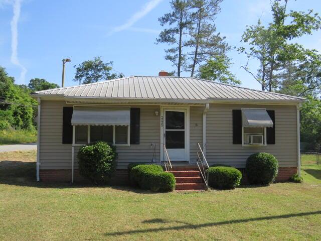 view of front of home with cooling unit, metal roof, and a front lawn