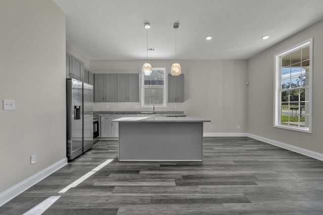 kitchen featuring light stone countertops, stainless steel refrigerator with ice dispenser, decorative light fixtures, a center island, and gray cabinets