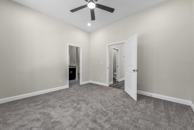 unfurnished bedroom featuring dark colored carpet, ensuite bath, and ceiling fan