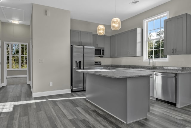 kitchen with light stone countertops, a center island, sink, stainless steel appliances, and gray cabinets