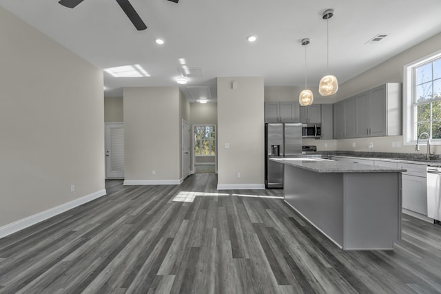 kitchen with light stone countertops, gray cabinetry, stainless steel appliances, sink, and a center island