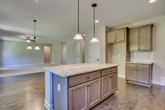 kitchen with ceiling fan, hanging light fixtures, light stone counters, decorative backsplash, and a kitchen island