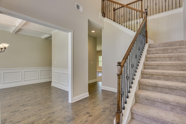 stairway featuring hardwood / wood-style flooring, a notable chandelier, crown molding, and beamed ceiling