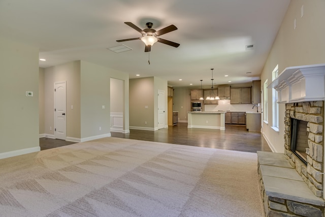 unfurnished living room featuring a fireplace, dark carpet, ceiling fan, and sink