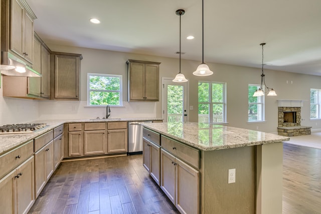 kitchen with sink, hanging light fixtures, stainless steel appliances, a stone fireplace, and a kitchen island