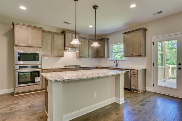 kitchen featuring light stone countertops, a kitchen island, decorative light fixtures, and appliances with stainless steel finishes