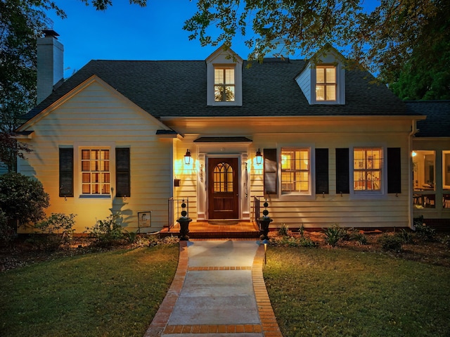 cape cod-style house featuring a shingled roof and a front yard