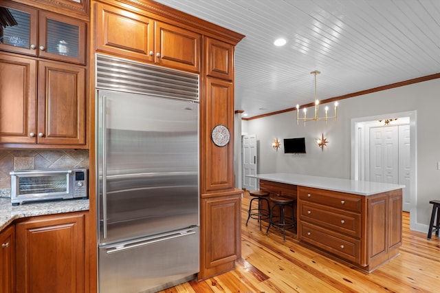 kitchen featuring built in fridge, ornamental molding, brown cabinetry, and light wood-style flooring