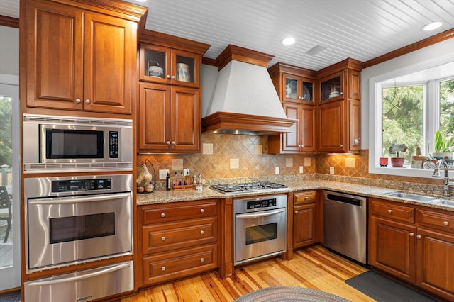 kitchen with appliances with stainless steel finishes, a warming drawer, a sink, custom exhaust hood, and brown cabinets