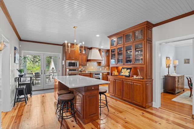 kitchen featuring stainless steel appliances, premium range hood, brown cabinetry, light wood finished floors, and a breakfast bar