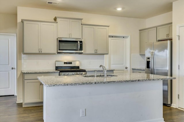 kitchen with sink, dark wood-type flooring, stainless steel appliances, light stone counters, and a center island with sink