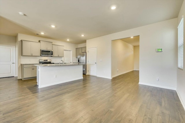 kitchen featuring gray cabinetry, a kitchen island with sink, sink, light stone countertops, and stainless steel appliances