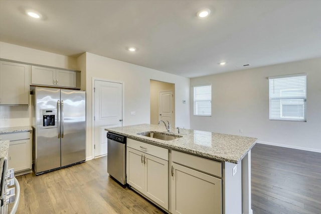 kitchen featuring sink, a healthy amount of sunlight, stainless steel appliances, light stone counters, and a kitchen island with sink