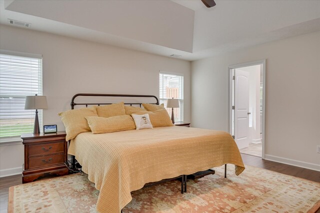 bedroom featuring visible vents, baseboards, ensuite bath, and wood finished floors