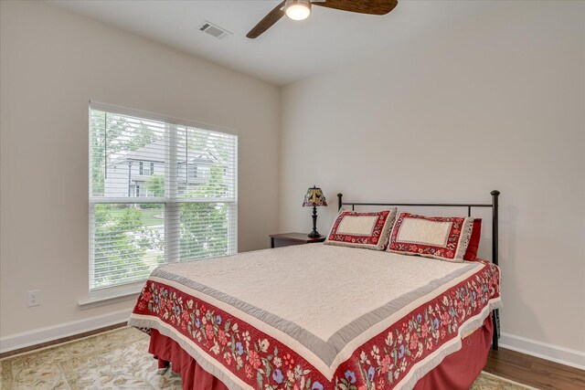bedroom featuring baseboards, wood finished floors, visible vents, and multiple windows