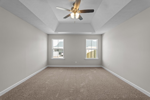 carpeted spare room featuring a healthy amount of sunlight, ceiling fan, and a tray ceiling