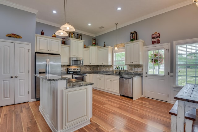 kitchen featuring stainless steel appliances, decorative light fixtures, a center island, and dark stone counters