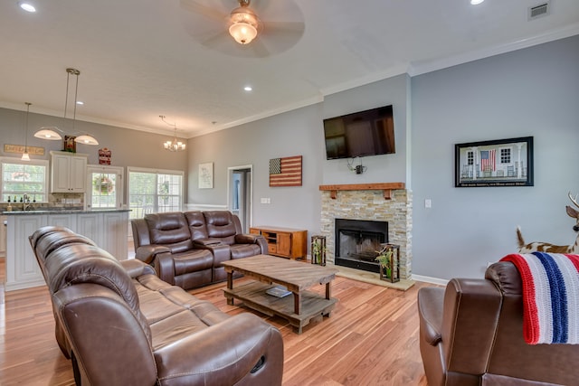 living room featuring sink, crown molding, light wood-type flooring, a fireplace, and ceiling fan with notable chandelier