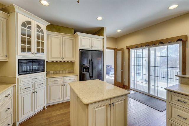 kitchen featuring light wood-type flooring, black appliances, light stone counters, recessed lighting, and glass insert cabinets