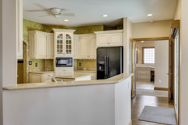 kitchen featuring black appliances, a ceiling fan, wood finished floors, recessed lighting, and glass insert cabinets