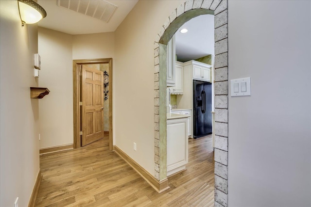 corridor featuring arched walkways, visible vents, light wood finished floors, and baseboards