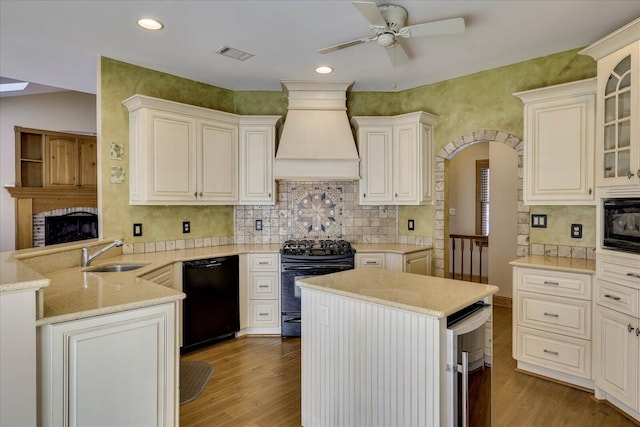 kitchen featuring black appliances, a sink, wood finished floors, arched walkways, and custom exhaust hood