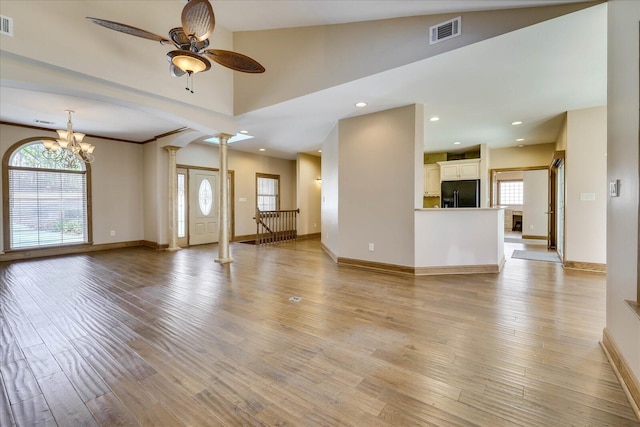 unfurnished living room featuring light wood finished floors, visible vents, baseboards, ceiling fan with notable chandelier, and ornate columns