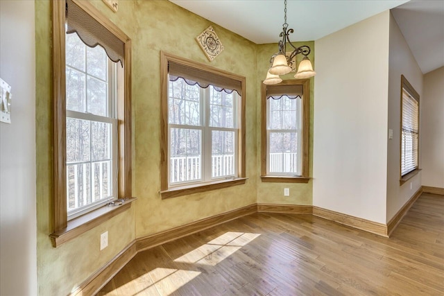 unfurnished dining area with a notable chandelier, wood finished floors, and baseboards