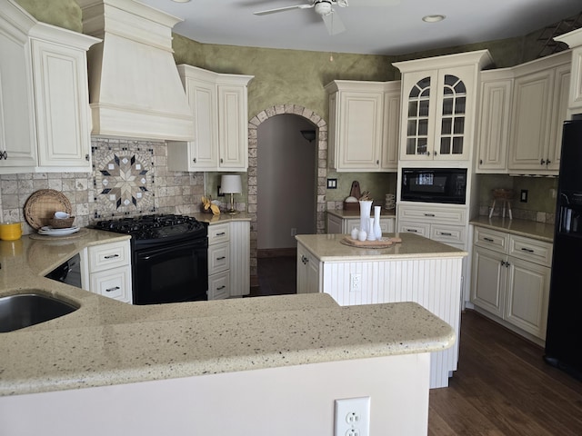 kitchen featuring black appliances, light stone counters, premium range hood, and dark wood-style flooring