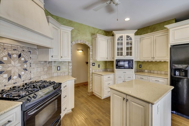 kitchen featuring black appliances, custom exhaust hood, arched walkways, and light wood-type flooring