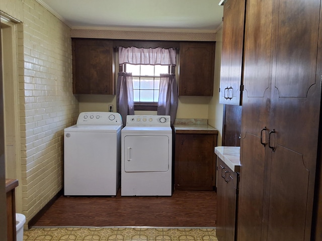 laundry area with brick wall, washer and dryer, cabinet space, dark wood-style floors, and crown molding