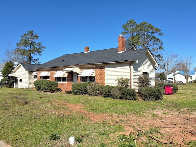 rear view of property with brick siding, roof with shingles, a chimney, and a yard