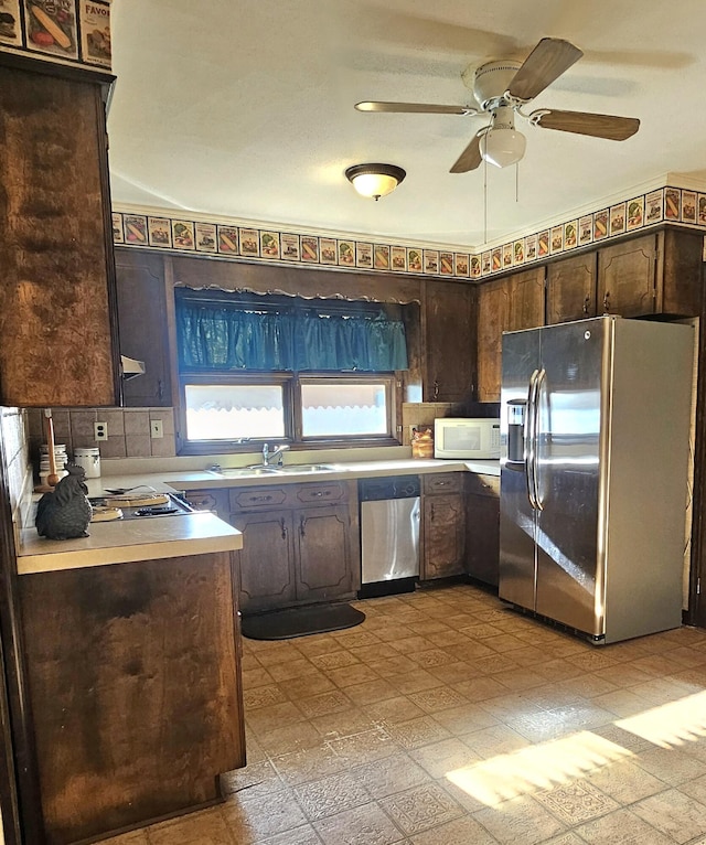 kitchen with dark brown cabinetry, light countertops, stainless steel appliances, light floors, and a sink