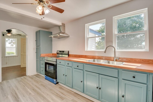 kitchen with stainless steel range with electric stovetop, wall chimney range hood, sink, and wooden counters