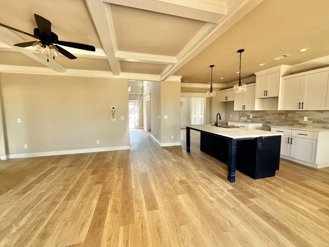 kitchen featuring a kitchen island with sink, a sink, light wood-style floors, open floor plan, and backsplash