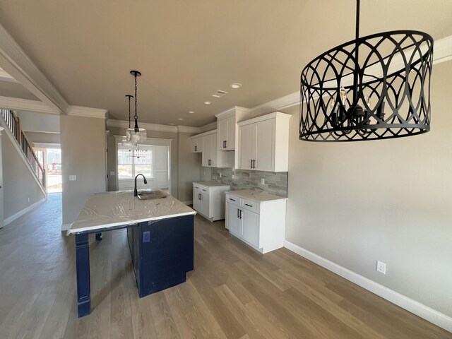 kitchen with a sink, white cabinetry, ornamental molding, light wood-type flooring, and backsplash