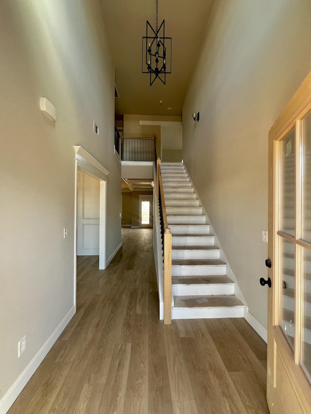 stairs featuring visible vents, baseboards, a towering ceiling, wood finished floors, and a notable chandelier