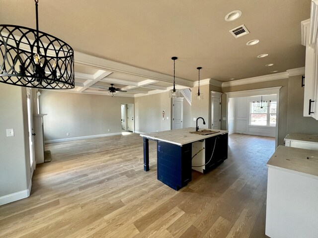 kitchen with light countertops, a ceiling fan, open floor plan, a sink, and coffered ceiling