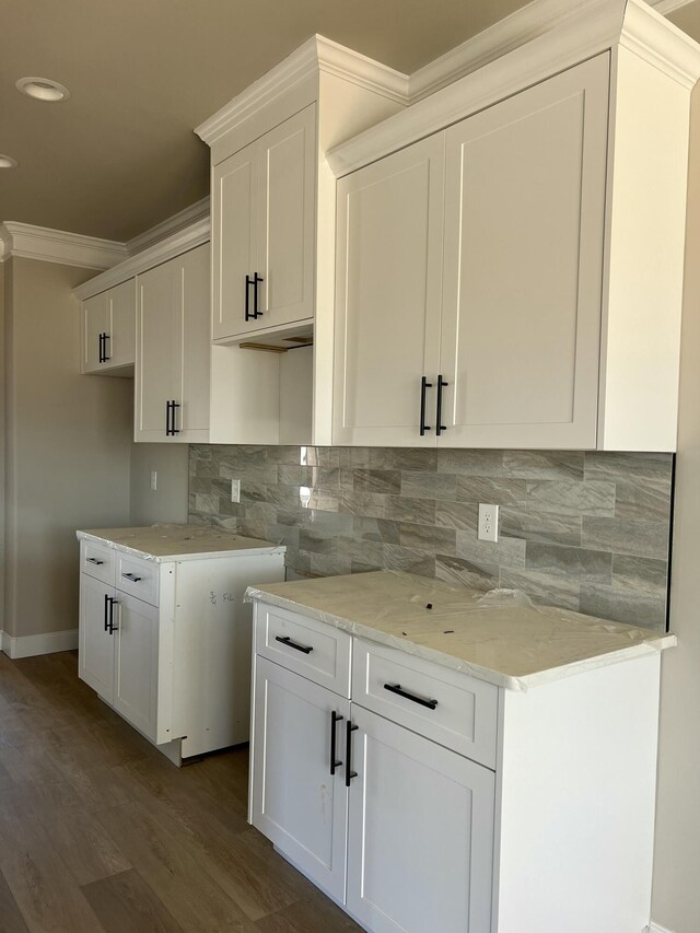 kitchen featuring dark wood-style flooring, tasteful backsplash, ornamental molding, white cabinets, and light stone countertops