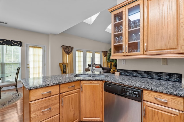 kitchen featuring dark stone counters, a wealth of natural light, stainless steel dishwasher, and a sink