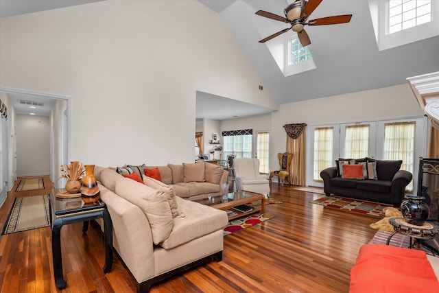 living room with high vaulted ceiling, ceiling fan, visible vents, a skylight, and wood finished floors