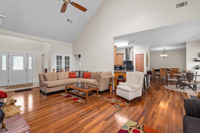 living area with visible vents, hardwood / wood-style flooring, high vaulted ceiling, and ceiling fan with notable chandelier