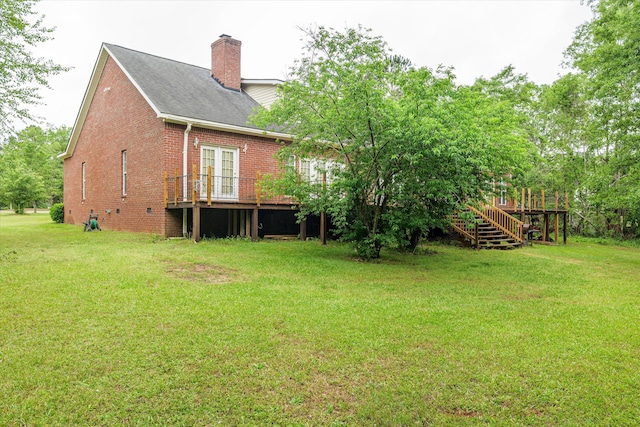 rear view of property with a chimney, brick siding, a wooden deck, and a yard