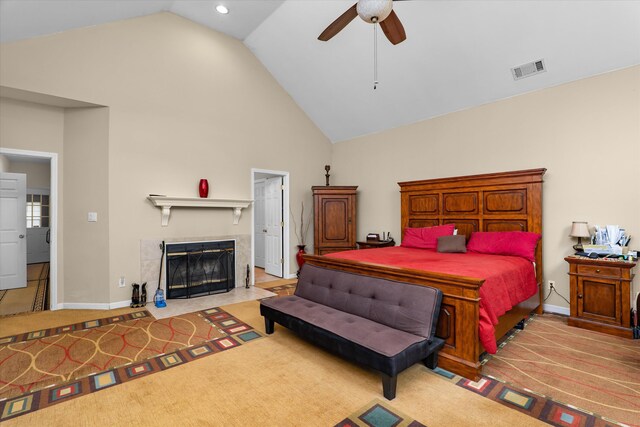 carpeted bedroom featuring a tiled fireplace, ceiling fan, baseboards, visible vents, and high vaulted ceiling