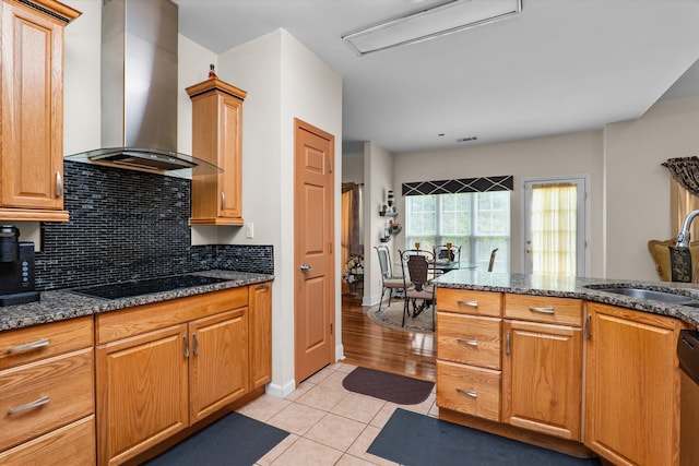 kitchen featuring wall chimney range hood, tasteful backsplash, black electric stovetop, a sink, and light tile patterned flooring