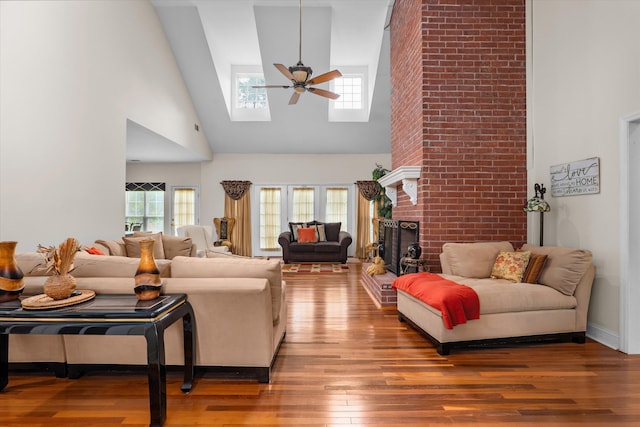 living area with a brick fireplace, high vaulted ceiling, a ceiling fan, a skylight, and wood finished floors
