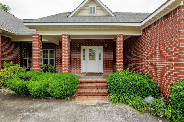 property entrance with a porch, roof with shingles, and brick siding