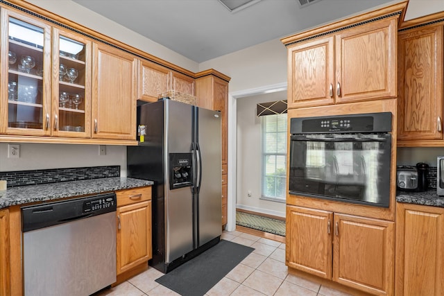 kitchen with dark stone countertops, stainless steel appliances, glass insert cabinets, and light tile patterned flooring